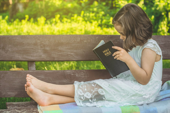 Reading the Holy Bible in outdoors. Christian girl holds bible in her hands sitting on a bench. Concept for faith, spirituality and religion. Peace, hope