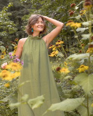 Woman in green dress holds wild flowers bouquet in a park or forest. Romantic idea for a book cover, summer inspitation