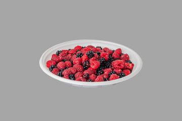 Fresh raspberries and blackberries on a white plastic plate. Clipping path.