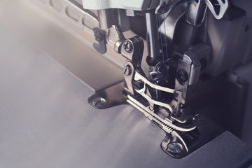 Mechanism of an industrial overlock sewing machine - closeup view in dark light mood on foot and needles with blurred background - copy space for text