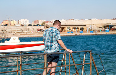 Fototapeta premium Portrait of tourist and traveler is posing and walking on beach pier, enjoys in sun and view of sea landscape. Man with sunglasses on vacation in summertime in hotel resort on sea jetty platform.