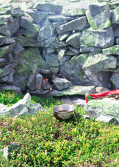 hiking kettle on the bonfire between big stones, stones wall on the background, cup of coffe on the foreground