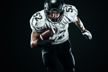 American football sportsman player in helmet isolated run in action on black background. Sport and...