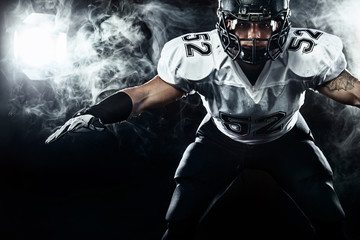 American football sportsman player in helmet on black background with smoke. Sport and motivation...