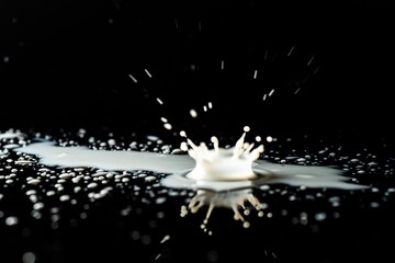 Milk spilled on black surface, closed up, selective focus - obrazy, fototapety, plakaty