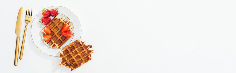 panoramic shot of cutlery near waffles with strawberries on plate on white