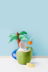 Fresh coconut on a pastel blue background with coconut tree inflatable drink holder, summer vibes concept with copy space