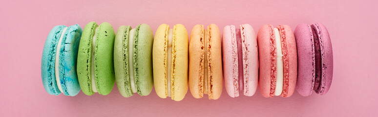 top view of colorful fresh delicious French macaroons in line on pink background, panoramic shot