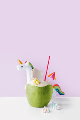 Fresh coconut on a pastel purple background with unicorn inflatable drink holder, summer vibes...