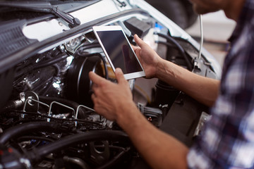 Close up of a man using his tablet to know how to fix car engine.