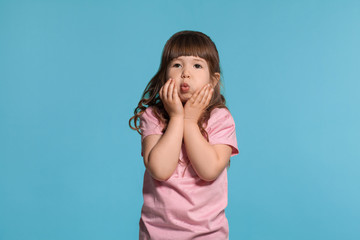 Beautiful little girl wearing in a pink t-shirt is posing against a blue studio background.