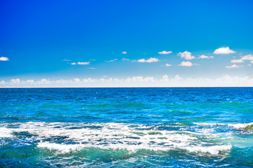 Fototapeta na wymiar Seascape with blue water surface, calm waves, bright sky and white clouds