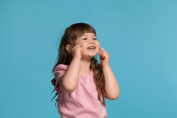 Beautiful little girl wearing in a pink t-shirt is posing against a blue studio background.