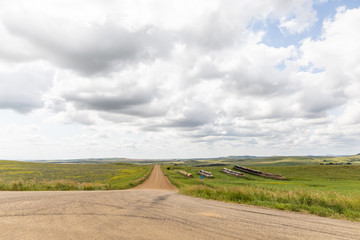 a long dirt road in rural North Dakota with a bright blue sky with clouds in the horizon