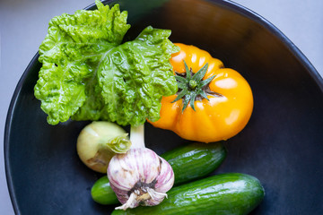 Set of various fresh vegetables in black bowl - cucumber, yellow tomato, onion, garlic, basil leaf - fresh ingredients for healthy eating.