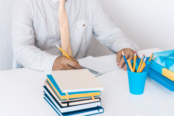 man in white shirt and yellow tie making notes on modern stylish work place with office supplies, glasses, notebooks and books, desk work concept in white and blue colors.