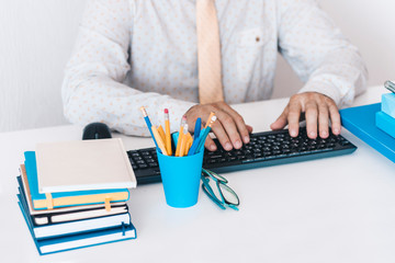 man in white shirt typing on keyboard laptop computer, plastic blue holder with pencils and pens,...
