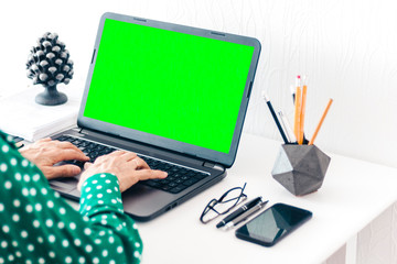 woman typing on keyboard green screen laptop, concrete holder with pencils and pens, notebook,...