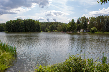 Beautiful summer landscape of blue sky in the clouds and a picturesque lake, surrounded by coniferous and deciduous forest.