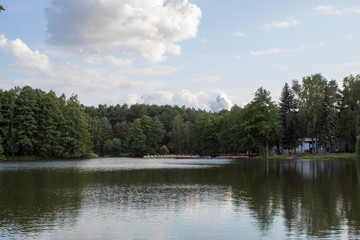 Beautiful summer landscape of blue sky in the clouds and a picturesque lake, surrounded by coniferous and deciduous forest.