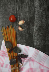 spaghetti, basil, peppercorn garlic, cherry tomatoes on black wooden background - flat lay. Image contains copy space