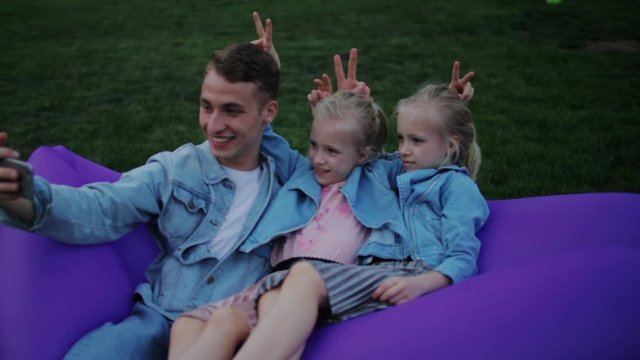 gentleman and little girls take selfie holding fingers near heads sitting in inflatable lounger closeup slow motion