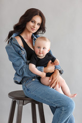 Young woman mother in denim overalls holds a baby child in her arms. White background in the studio.Mother with baby isolated on white. Mothers Day, love family, parenthood childhood concept. Happy fa