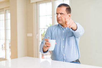 Middle age man drinking coffee in the morning at home pointing with finger to the camera and to you, hand sign, positive and confident gesture from the front