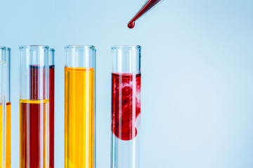 Laboratory test tubes with red and yellow liquids on light blue background