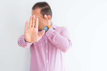 Middle age man wearing business shirt over white wall covering eyes with hands and doing stop gesture with sad and fear expression. Embarrassed and negative concept.