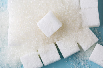 Heap of granulated sugar with cube on blue background. 