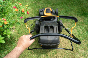 Man hand holding a lawn mower machine to cutting green grass