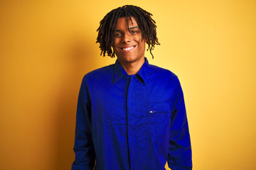 Afro worker man with dreadlocks wearing mechanic uniform over isolated yellow background with a happy and cool smile on face. Lucky person.