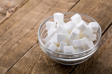 Closeup of sugar cubes in glass bowl on wooden table.