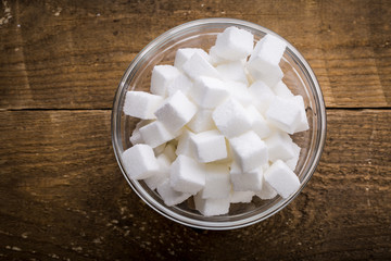 Closeup of sugar cubes in glass bowl on wooden table.