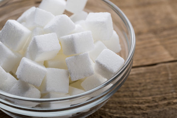 Closeup of sugar cubes in glass bowl on wooden table.