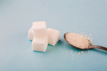 Granulated sugar in spoon with cube on blue background.