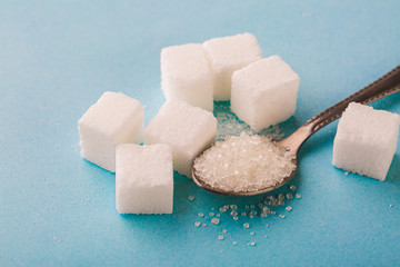 Granulated sugar in spoon with cube on blue background.