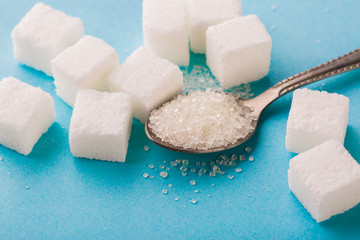 Granulated sugar in spoon with cube on blue background.