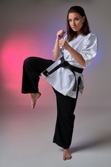 Athletic woman in traditional kimono is practicing karate in studio.