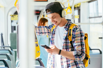 Young man is standing in a bus with headset on his head and listening to the music.