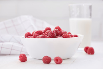 Ripe raspberries in white bowl and glass of milk.