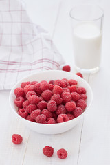 Ripe raspberries in white bowl and glass of milk.