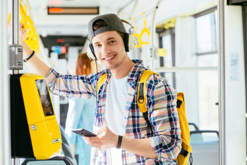 Young man is standing in a bus with headset on his head and listening to the music.