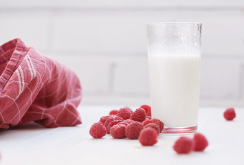 Glass of milk and ripe raspberries. White background.