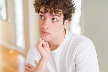 Young handsome man wearing white t-shirt with hand on chin thinking about question, pensive...