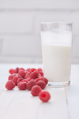 Glass of milk and ripe raspberries. White background.
