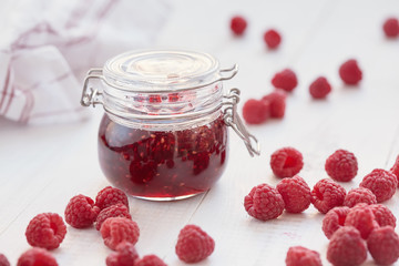 Raspberry jam in a glass jar on white table
