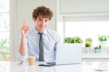 Young business man working with computer laptop at the office surprised with an idea or question pointing finger with happy face, number one