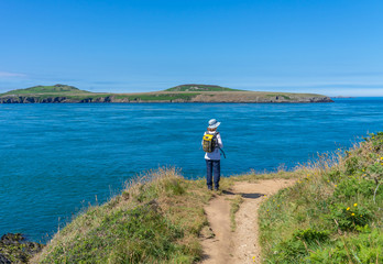 Fototapeta na wymiar Lone adventurer standing on the cliff top in St Justinians looking out over Ramsey Sound towards Ramsey Island RSPB nature reserve